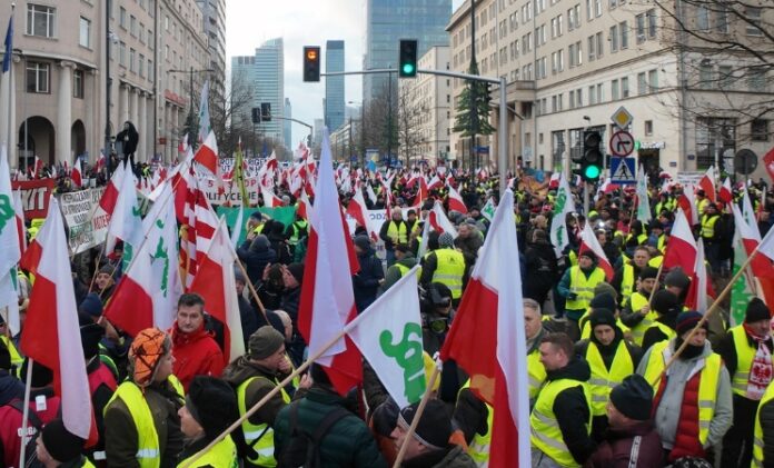 Na zdjęciu protestujący związkowcy i rolnicy, którzy zablokowali centrum Warszawy. Ubrani są w żółte koszulki, a w dłoniach mają flagi polski.